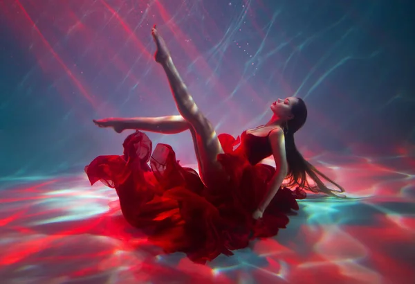 Fantasy woman drowning at bottom of ocean sea beauty ballerina girl swimming posing underwater sexy long legs red dress floating soars. Magic divine light. Art Creative shooting lady under water pool