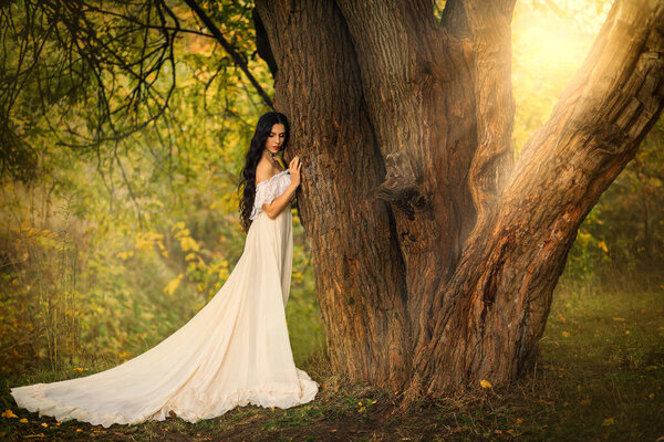 Mystery art portrait fantasy woman in white vintage style dress. queen walking in summer forest hand touching tree. Girl princess long dark hair. Victorian romantic lady dreams of love. Green nature.