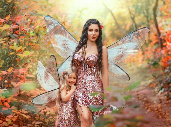 fantasy pixie woman mother and happy daughter little fairy girl walking together in autumn forest. Concept family love caring. Butterfly wings costume creative pink shiny dress. Orange trees Art photo