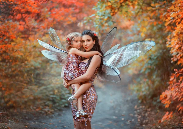 幻想的な女性の妖精 彼女の腕の中で女の子を保持 母と娘 カメラを見て幸せな顔を抱いている 妖精のカーニバルの衣装蝶の翼 光沢のあるピンクの一致するドレス 家族撮影 — ストック写真