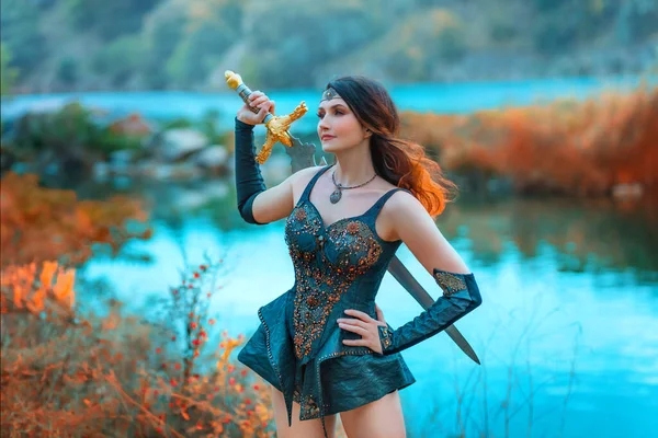 Fantasy woman viking princess warrior. Warlike girl Amazon Lady nordic style sexy valkyrie goddess holding sword in hand. Leather costume armor red hair flies in wind. Autumn orange nature blue river