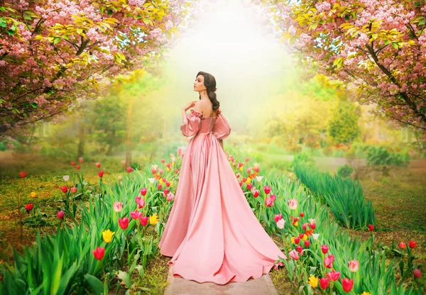 春の庭の花のチューリップ桜の木緑の草の古い路地を歩く幻想的な女の子の王女 女性の女王で長い豪華なロイヤルピンクのドレスとともに電車パフスリーブヴィンテージスタイルのアート写真 — ストック写真