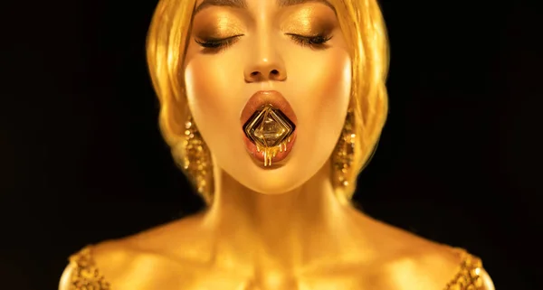 Portrait closeup Beauty fantasy woman sexy mouth hold diamond liquid gold drops drip on lips face in golden paint shiny skin. Fashion model sexy girl metallic makeup. creative jewellery. black studio.
