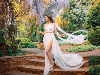 Fantasy woman greek goddess walks in spring garden purple flowers green tree nature day sun light. Sexy girl queen antique style white silk dress fly, gold diadem on red hair, lady going down stairs. clipart