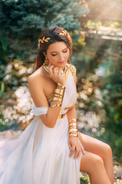 艺术照幻想中的希腊女神像坐在春天的花园里 绿树青草 天日魔法阳光下 性感少女女王古式白色丝裙 金项链手镯冠带 — 图库照片