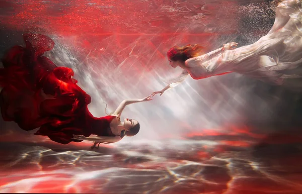 カップル2人の女性が水中で 少女ファンタジー人魚川ニンフ 長いドレスの尾絹の生地なびかせ泳ぐ 女性妖精ギリシャの女神は水の下で溺れる プールの赤い光の服に身を包んだファッションモデル — ストック写真