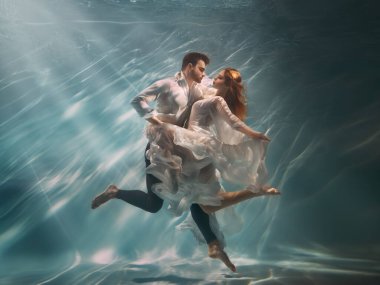 Gerçek İnsanlar sanat fotoğrafı. Aşık mutlu çift suyun altında yüzer, kadın ilham perisi erkek şair yaratıcıya ilham verir. Nymph kızı denizin dibindeki adamla dans ediyor. Kızıl saçlı, beyaz, uzun, ipek elbiseli..