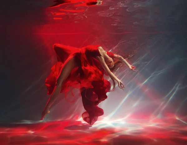 穿着性感腿的时装模特 幻想中的女子在水底跳舞 红丝长裙面料飘扬 Belerina仙女舞者在黑暗的深水池中游泳水下射击艺术魔法灯 — 图库照片
