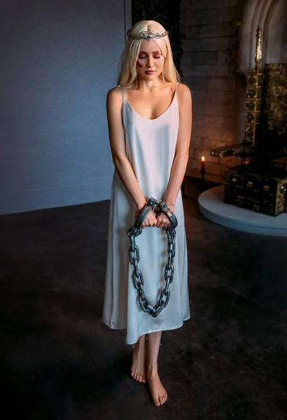 portrait fantasy woman princess hands in chains prison handcuffs steel chain shackles. White nightgown vintage style. Mystery scared Bare feet girl queen slave wound scars blood on face. dark room.