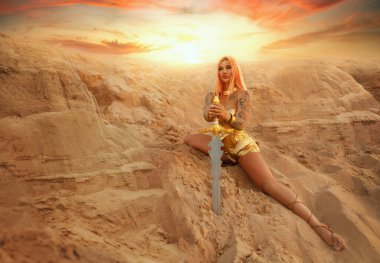 Fantezi kadın savaşçı yaratıcı kostüm savaşçısı seksi kız tanrıça. Altın zırh metal korse, beyaz Yunan tarzı fantastik elbise. Bayan Elf elinde kılıç tutuyor. Kum çölünde gökyüzünde moda modeli.