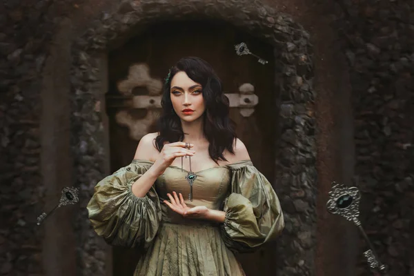 Fantasy portrait woman princess keeps secret holds old key to all doors in hands. Background old wall, wooden door. Medieval Girl Vintage Golden Ancient Style Dress. keys fall hovering floating in air
