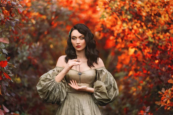 art photo portrait real people fantasy woman queen keeps secret holds old key to all doors in hands. autumn nature red orange leves tree foliage. Medieval Girl princess Vintage Ancient Style Dress