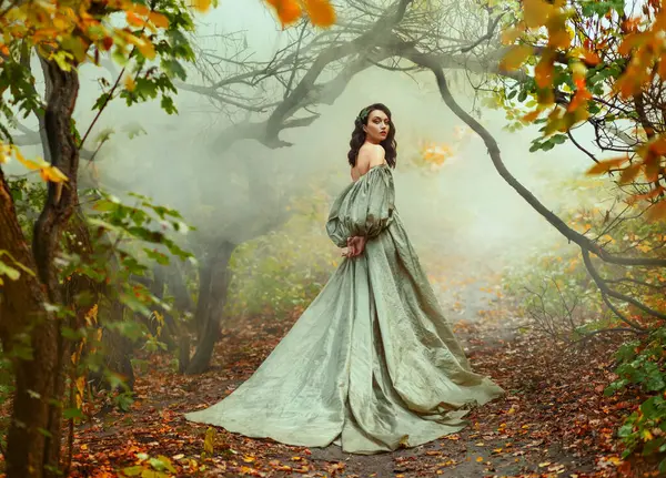 Photo real people fantasy woman walks in mystical autumn misty forest orange foliage trees mist smoke. Dark Hair beauty face princess girl looking back. Medieval royal vintage long green dress train.