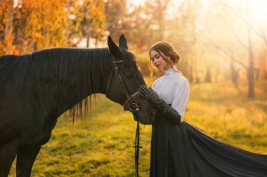 Fantezi kadın atını okşuyor. Mutlu yetişkin kız güzellik makyajlı asil bayan. Aşk evcil hayvanı. Yaz doğa ormanı kutsal güneş ışığı. Uzun ipek siyah elbise, eski tarz. resim gerçek kişi.