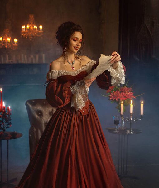 Художественный портрет Готической Фантазии Королевы вампиров, держащей в руках бумажное письмо. Карнавальный вечер праздничное белое красное платье Хэллоуин костюм черные волосы. Счастливая девушка вампир сексуальное лицо губы острые клыки зубы.