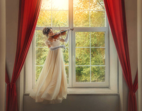 Искусство фото реальный человек. Скрипачка-фантазёрка играет на скрипке в классическом старом стиле. Девушка стоит на подоконнике зеленый сад солнечный свет. Сексуальная леди красотка лицо белое винтажное платье муха ветер дуновение