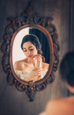 Antika bir aynanın sanat fotoğrafı yansıması. Ortaçağdan güzel bir kadın. Uzun saçlı, zarif bir kadın. Eski tarz beyaz Victoria tarzı çıplak omuzlar. Fantezi seksi prenses aynaya bakıyor.