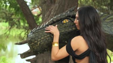 Portre sanatı Fantezi kadın savaşçı kraliçe elini okşuyor ejderha başına dokunuyor hayvan hayvanını sevgiyle besliyor. Peri Elf Kara Kraliçe Bauty Surat Tanrıçası. Yaz ormanı yeşili ağaçlar. Siyah elbise 4K.