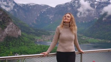 Gözlem güvertesinde gülümseyen mutlu bir kadın. Kız turist, Hallstatte Gölü 'nün manzarasının keyfini çıkarıyor. Seyahat eden kişi yeşil doğa gökyüzü bulutları. Dağlar Avusturya Gölü Turizm Köyü Hallstatt