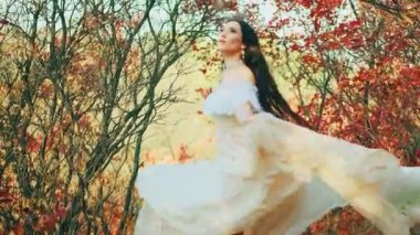 Fantezi mutlu kadın ormanda dans ediyor. Dansçı kız Prenses güzel, gülen surat. Beyaz, uzun, ipek kumaş kumaş elbise rüzgarda uçuşan saçlar. Sonbahar doğası kırmızı ağaçlar 4k