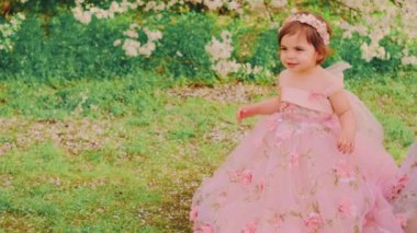 Portre Küçük mutlu, güzel, neşeli, neşeli kız pofuduk pembe elbiseyle dans ediyor. Gülen yüzlü çocuk prenses balo elbisesi tarzı. Arka planda bahar doğası çiçek açan beyaz ağaç yeşili çimenler.