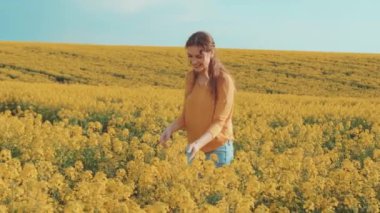 Neşeli, genç ve güzel bir kadın ayakta duruyor. Kokusunu alıyor. Sarışın kız kolza tohumu tarlasını, güneşli doğayı, bahar ağaçlarını sever. Turuncu ceket, kot pantolon. Arkaplan mavi parlak gökyüzü