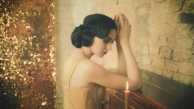 Genç, güzel, çekici, üzgün kadın yaşlı piyanoyu tutuyor. Kadın esmer, el sallayan saç stili. Altın lüks zengin elbisesi. Mum romantik bir şekilde yanar. Arkaplan odası. Parlak, parlak ekran tuğla duvar. 