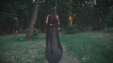 Gürültülü video. Silüet fantezi kadın Medusa gorgon Yunan tanrıçası. Siyah karnaval kostümü. Karanlık ormanda yürüyen gotik kız. Başında yılanlar, korkunç saçlar, siyah ipek elbiseler, gotik kraliçenin arkadan görünüşü.
