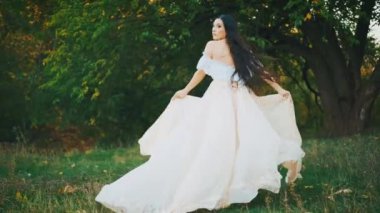 Fantezi mutlu kadın yeşil orman ağacı çayırında koşar. Prenses kız, siyah saçlı, beyaz, eski moda elbiseler rüzgarda uçuşuyor. Arkadan bakan kadın yavaş çekimde. Sonbahar doğa çim ağaçları çimenler