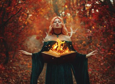 Gerçek sanat fotoğrafçısı. Fantezi kadın cadı büyüsü sihirli bir kitap yaratıyor havada süzülüyor, alev alev yanıyor. Elf kız ellerini kaldırdı. yeşil uzun elbiseler rüzgar esintisi. orman ağaçları turuncu kırmızı yapraklar.