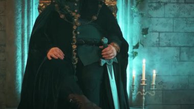 Ortaçağ 'dan kalma güçlü bir adam eski bronz tahtta oturuyor elinde kılıç, zalim kral imajı var. Karnaval kostüm kadife kıyafetler Kraliyet altın tacı, mücevherler. Ciddi düşünceli surat. Gotik kale odası..