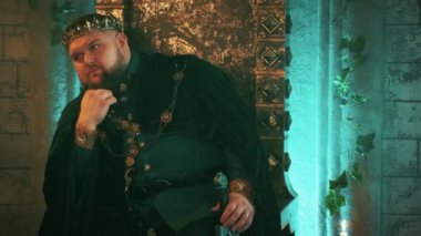 Savaşçı ortaçağ cesur güçlü adamı eski bronz tahtta oturur, zalim kral imajı çizer. Karnaval kostüm kadife kıyafetler kraliyet tacı, mücevherler. Ciddi düşünceli surat. Gotik kale odası..