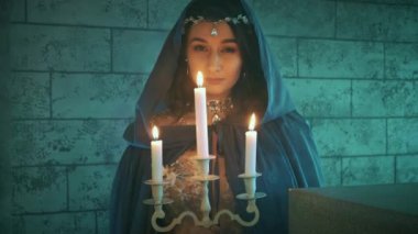 Gecenin karanlığında elinde mumlarla elinde şamdanla dolaşan güzel mistik kadın bir hayalet. Ortaçağ kraliçesi, mavi elbiseli, başlıklı, gotik elbiseli. Korku sanatı konsepti Cadılar Bayramı.