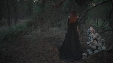Tahıllı gotik sanat filmi. Siyah, eski, uzun elbiseli bir hayalet kadının karanlık, mistik silueti. Birçok insanın kafatasının yanında putperest bir kadın var. Vampir ormanın derinliklerinde yürüyor. Arka görünüm
