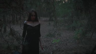 Gürültülü gotik sanat filmi. Yetişkin gotik kızın karanlık, mistik silueti. Dudaklarında kan olan vampir bir kadın alacakaranlık ormanında yürüyor. Siyah ortaçağ elbisesi. Doğa, ağaç.
