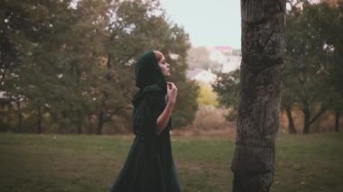 Gürültülü Gotik Video. Başlıklı yeşil pelerinli fantezi kadın prenses ahşap putperest putlara dua ediyor. Arka plan karanlık, mistik ormanlar. Ortaçağ cadı kraliçesi. Uzun kadife pelerin