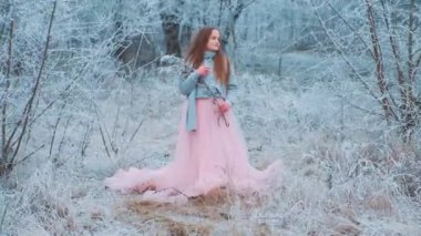 Güzel, kızıl saçlı, tatlı bir kız. Arkaplanda poz veriyor. Buz gibi karlı ormanda. Ellerinde buz ağacı dalı tutan bir genç. Sıcak mavi kazak, pembe lüks klasik etek elbise, tren.