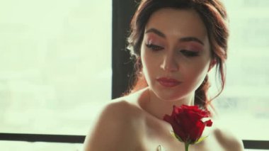 Yakından genç, çekici, güzel bir kadının portresi. Seksi çıplak omuzlar. Akşam makyajı, pembe dudaklar, siyah kaşlar, güzel kediler gri gözler, takma kirpikler. Esmer kız kırmızı gül tutuyor. tavan arası penceresi