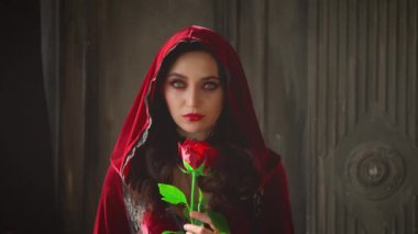 Mahalledeki gizemli, genç, gotik kadın. Cadılar bayramı vampir makyajlı kadın yüzü. Seksi moda kadife klasik kırmızı elbise. Kız Rose 'u elinde tutuyor. Karanlık oda, ortaçağ kalesi.