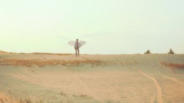 Yalnız fantezi kralı. Efsanevi genç kutsal kutsal seksi melek adam kumlu çölde yürüyor. Tanrı 'yı koruma kavramı. Beyaz kanatlar, kuş tüyleri. Açık gökyüzü, güneşli gün batımı, ağaçlar. Peri masalı kanatlı elf prensi.