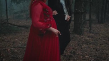 Siyah takım elbiseli gotik kadın el ele tutuşan gotik smokin giyen gotik bir vampir. Fantezi çift iki kişilik arka plan. Kırmızı elbise. Sis ormanı yaz yeşili doğa. Erkek, kız temalı düğünü sever.