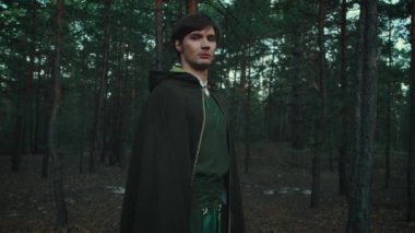 Fantazi genç erkek elf prensi karanlık gotik sık ormanda yürüyor. Gizemli siluet perisi adam. Büyücü adam cadı. Yaratıcı ortaçağ kıyafetleri pelerin yeşil kostüm. Moda modeli arka plan 