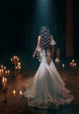 Sanat fotoğrafçısı gerçek bir fantezi kadın kar yağan odada duruyor, yukarıdan gelen sihirli ışık huzmesi, yanan mumlar, gece gotik odası. Dişi prenses, uzun, dar, dar, arkadan görünüşlü..