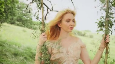 Genç ve güzel bir kadının portresi. Doğal sarışın, uçan, rüzgarda dalgalanan uzun saçlar. Sarışın kız orman prensesi gülen surat, yaz yeşili bahar doğasının tadını çıkar. Sallanıyor salıncakta