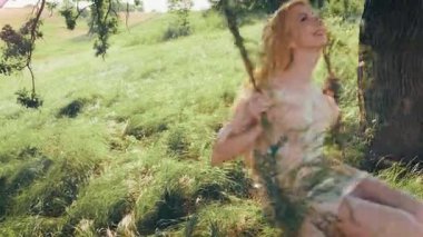 Genç mutlu sarışın kadın salıncakta sallanıyor. Sarı saçlı, uzun elbiseli ipek, rüzgârda uçuşan bir sinek. Neşeli kız model, gülen surat, hayatın tadını çıkar. Yaz mevsiminin tadını çıkar.