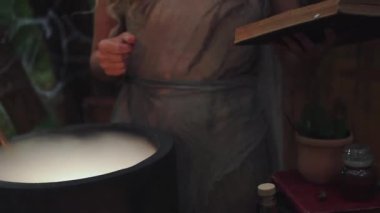 Orman doktoru karanlık güçlere karşı korunmak için ilaç yaratıyor, açık tüylü kıvırcık saçlı kadın sihirli güçlere sahip, başında çiçek çelengi olan yaşlı gri elbiseli kadın, kitaplı dekor ve test tüpleri olan kadın..