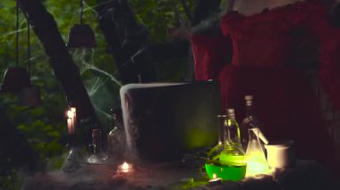 Gizemli video, orman büyücüsü kaynayan kazanda iksir yapıyor, damardan beyaz yoğun buhar akıyor, karanlık gecede şeffaf cam şişelerin yanında mumlar yanıyor, model yüzü yok..