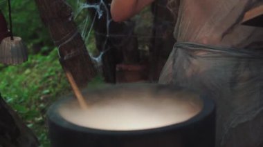 Sarı saçlı ve başında çiçek çelengi olan büyüleyici bir büyücü. Bayana şifalı bir ilaç hazırlıyor. Elinde kitap olan eski gri paçavra elbiseli bir kadın..