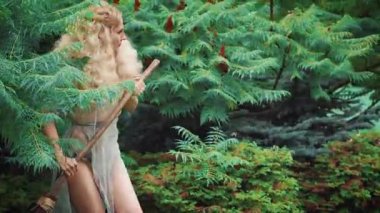 Ormandan komik, komik bir cadı çıkar ve kaşlarını çatar. Dallardan gelen eski bir süpürgenin ellerinde. Cadılar Bayramı partisinde baştan çıkarıcı bir cadının görüntüsü. Arka planda sonbahar bahçesi.