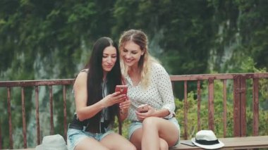 İki çekici kadın, tepede bir bankta oturmuş sohbet eden dağların resimli görüntüsüyle. Kız, fotoğraf arkadaşını cep telefonunda gösteriyor. Bağımlılık modern aletler. Mutlu Turistler Georgia Okace Kanyonu